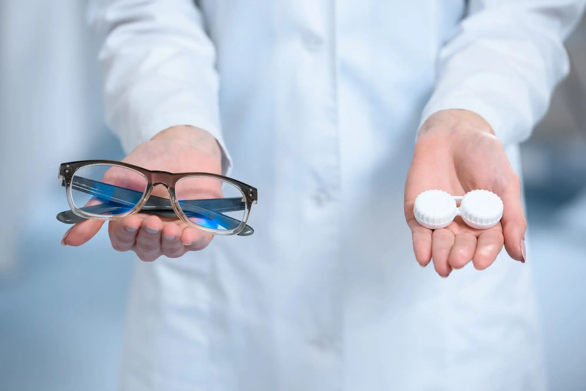 Lentes aéreos o lentes de contacto: ventajas y desventajas Lentes aéreos o lentes de contacto: un médico oftalmólogo sostiene unos anteojos en una mano y un estuche de lentes de contacto en la otra.