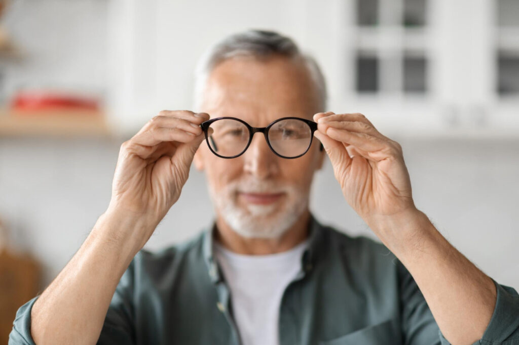 Paciente mayor sosteniendo sus anteojos en primer plano: una comparativa entre cirugía refractiva láser y lentes intraoculares para dejar de usar lentes